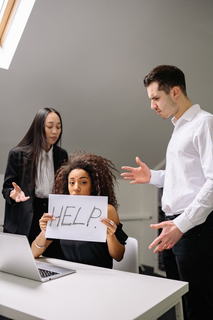 Woman holding HELP sign surrounded by colleagues in a tense office situation.
