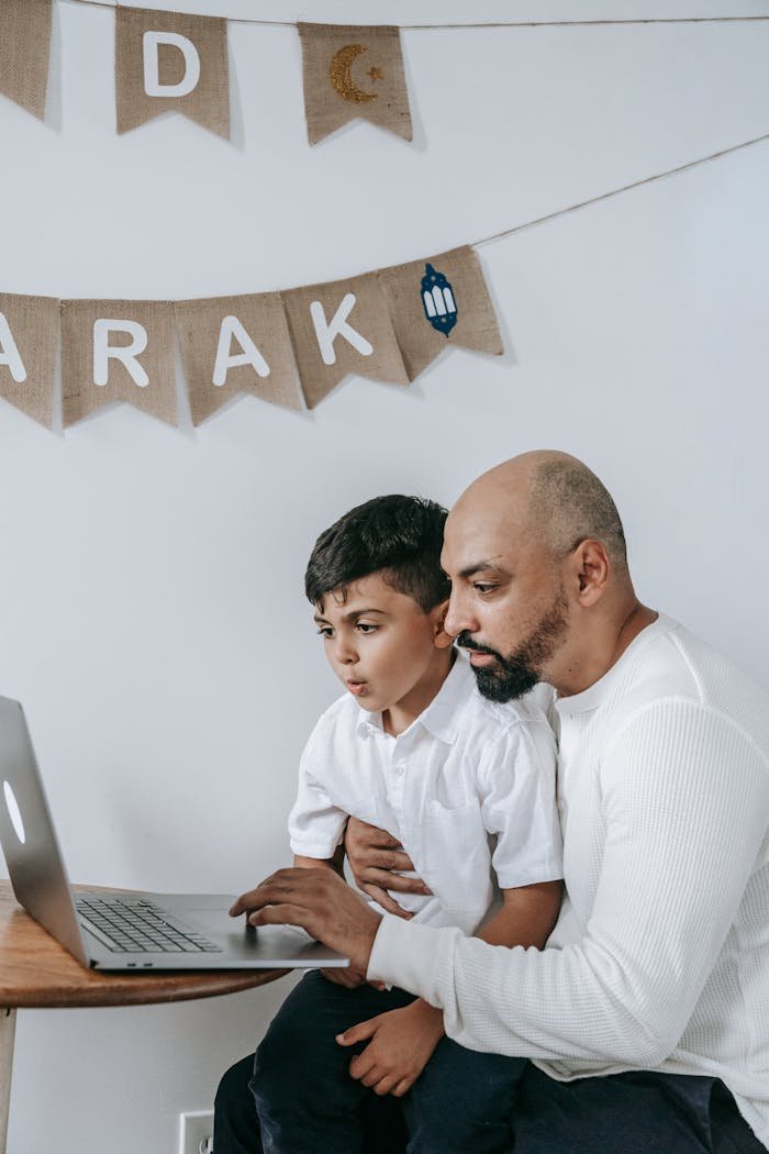 Father and son engaged with a laptop, sitting indoors with festive decorations.